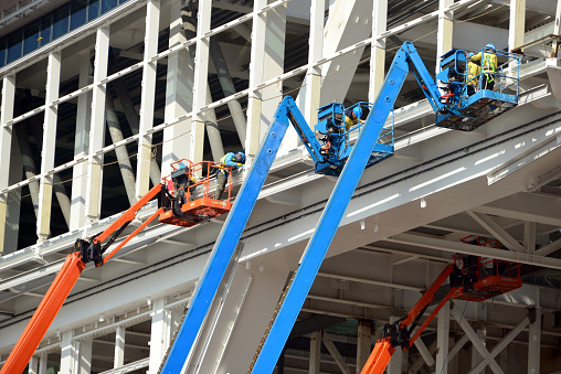 Hong Kong, China: specialized construction workers workers assemble a steel structure for a pedestrian bridge using telescopic boom lifts -  Hong Kong International Airport, Chek Lap Kok island.