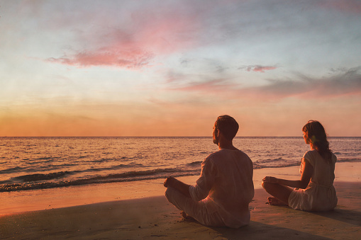 mindfulness, couple doing yoga and breathing exercises at sunset, meditation on the beach