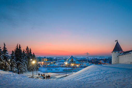 Street view of the city of Kazan in the evening. Winter cityscape, the ancient fortress wall of the Kazan Kremlin surrounding the central part of the city and modern buildings against the sunset.