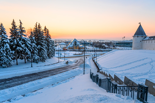 Street view of the city of Kazan in the evening. Winter cityscape, the ancient fortress wall of the Kazan Kremlin surrounding the central part of the city and modern buildings against the sunset.
