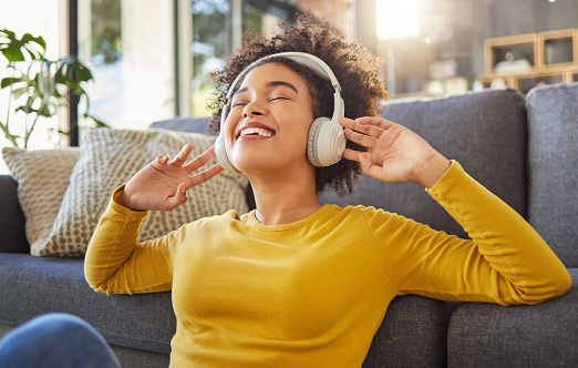 Young joyful mixed race woman wearing headphones and listening to music at home. One cheerful hispanic female with a curly afro enjoying music and sitting on the floor at home