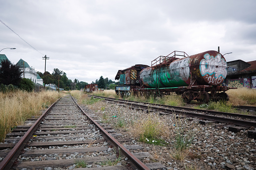 Osorno, Chile - February, 2020: Abandoned rail wagon with cistern covered in graffiti on railway tracks. Old railway station of Osorno on left. Abandoned railroad tracks with old rusty railway wagon