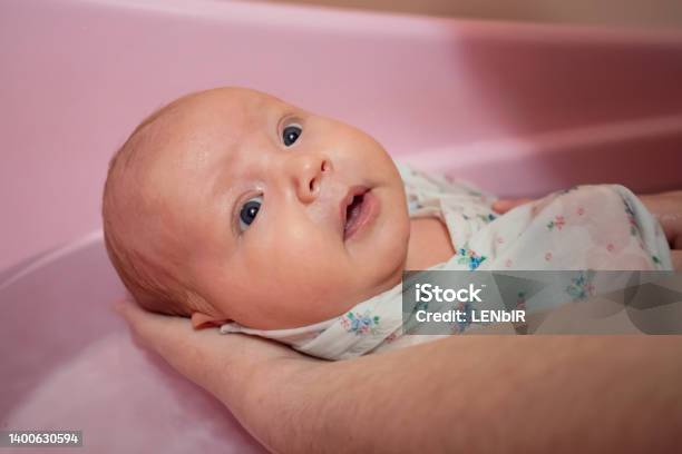 Mother Washes Newborn Baby In Pink Bath With Water At Home Stock Photo - Download Image Now