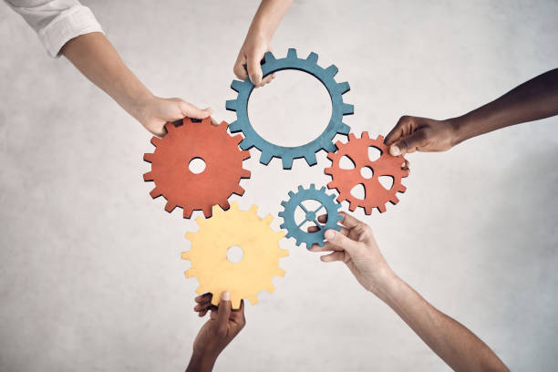 Group of five businesspeople holding and fitting gears together in an office at work. United business professionals having fun connecting gear pieces during a meeting Group of five businesspeople holding and fitting gears together in an office at work. United business professionals having fun connecting gear pieces during a meeting five people stock pictures, royalty-free photos & images