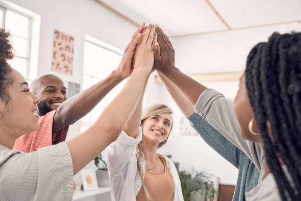 group of five happy diverse businesspeople giving each other a high five in an office at work. business professionals having fun joining their hands in support and unity during a meeting - excitement business person ecstatic passion imagens e fotografias de stock