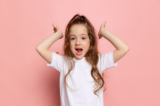 Wow, joy. Studio shot of cute little girl, kid wearing white t-shirt posing isolated on pink background. Concept of children emotions, fashion, beauty, school and ad concept.