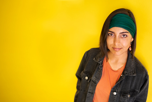 Portrait of a stylish young woman looking up and smiling while standing in front of a bright yellow background