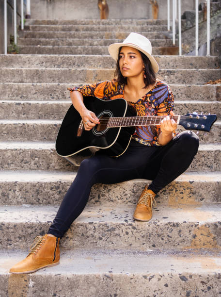 istock Young female musician strumming on a guitar outside on some steps 1400635174