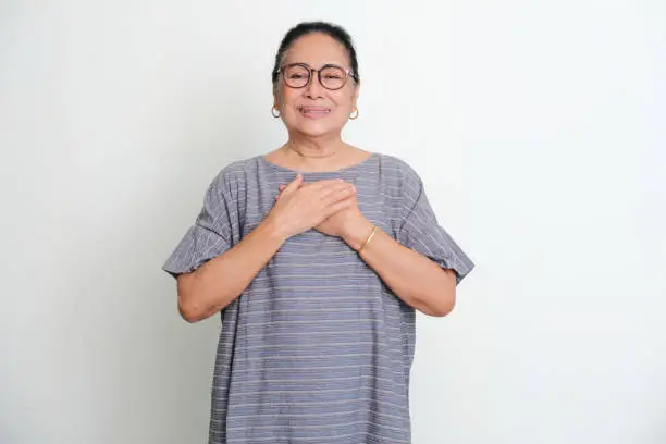 Elderly Asian woman showing grateful gesture with her hand touching chest