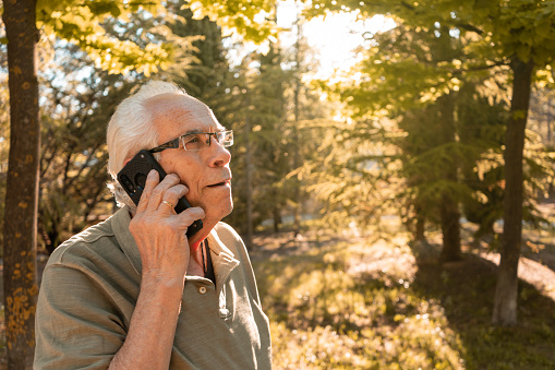 Portrait of older man calling by mobile phone, in the mountains, on a sunny day. Horizontal photography with copy space.