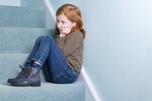 Cute auburn-haired girl of seven sitting on the stairs.