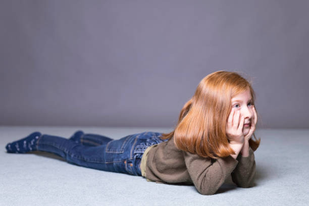 Pretty 7-year-old Caucasian girl with ginger hair and blue eyes looking at something off camera.
