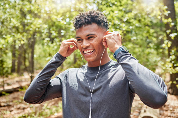 giovane atleta ispanico di razza mista in forma che ascolta musica mentre corre in una foresta fuori nella natura. l'esercizio fisico fa bene alla salute e al benessere. divertente, positivo, felice - real estate immagine foto e immagini stock