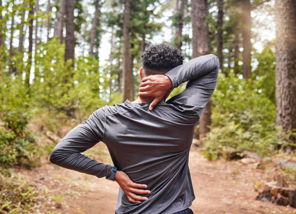 Unrecognizable mixed race hispanic male stretching before a run while experiencing some back and neck pain in a forest. Exercise is good for your health and wellbeing. Stretching is important to prevent injury and muscle strain Man holding his neck and back in pain while out for a run in the woods. Fit man experiencing discomfort in his body while exercising in a nature environment joint pain stock pictures, royalty-free photos & images