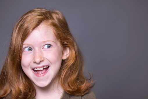 Pretty 7-year-old Caucasian girl with ginger hair and blue eyes looking excitedly off-camera.