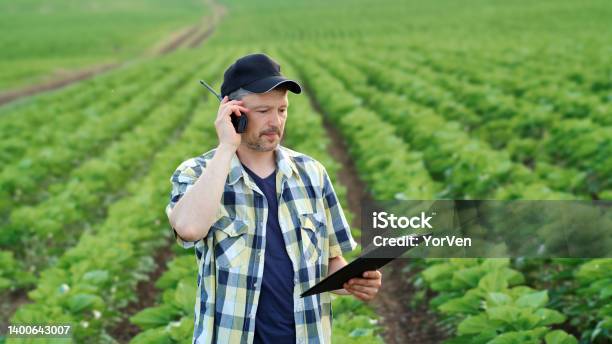 Male Farmer In Agricultural Field Holding A Clipboard And Talking On Walkietalkie Stock Photo - Download Image Now