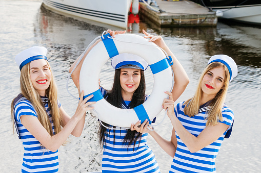 Cheerful girlfriends in striped dresses and shirts on a yacht in the summer. Happy young women of Caucasian appearance are resting. Tourism and travel concept