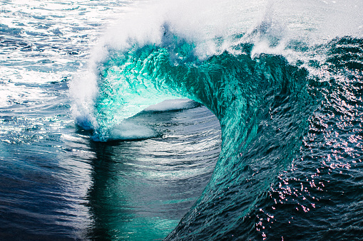 Close up of powerful and bright blue ocean wave barrelling on a shallow reef