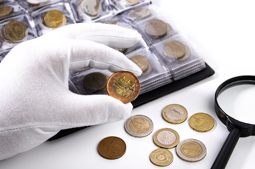 A collector in white gloves examines a coin, close-up.