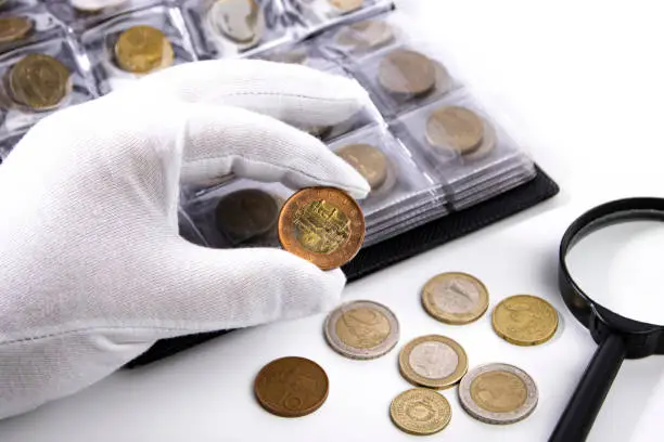 Photo of A collector in white gloves examines a coin, close-up.