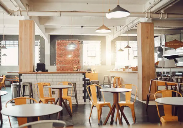 Photo of Interior of empty modern cafe or restaurant during the day. Round tables and yellow chairs in a rustic cafe. Open space coffee shop with exposed pipes and pendant hanging lights