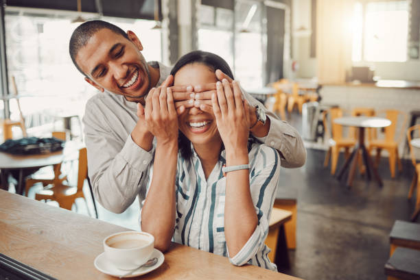 istock Cheerful young man covering his girlfriends eyes and surprising her while sitting in a cafe. Happy young mixed race couple meeting for coffee on their first date. Excited woman trying to guess who is behind her 1400648211