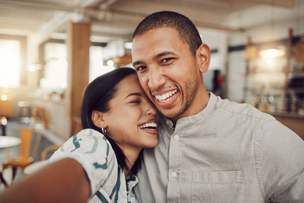 istock Loving young laughing and having fun while holding mobile phone to take a selfie in a cafe. Happy mixed race man and woman looking happy while sitting together on a date 1400648216