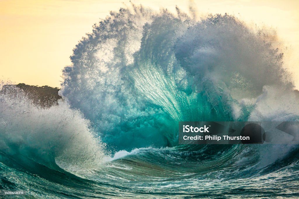 Powerful storm generated ocean swell exploding dangerously on the shoreline with soft golden sky Wave - Water Stock Photo