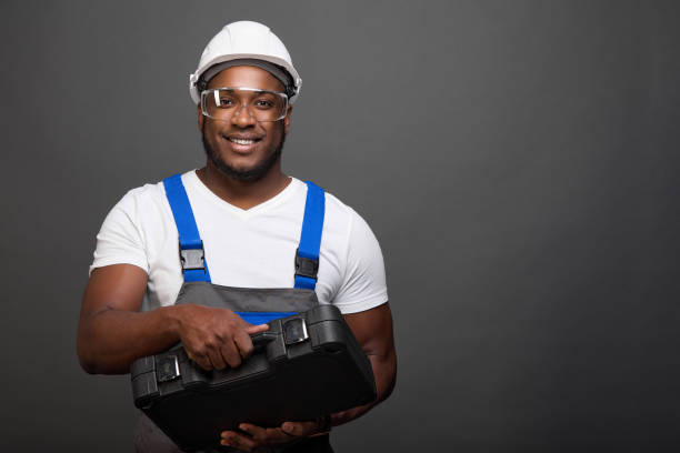 Satisfied foreman carpenter in protective glasses and a helmet holds in front of him a large set of professional tools in a drawer. A black construction worker poses with tools in his hands