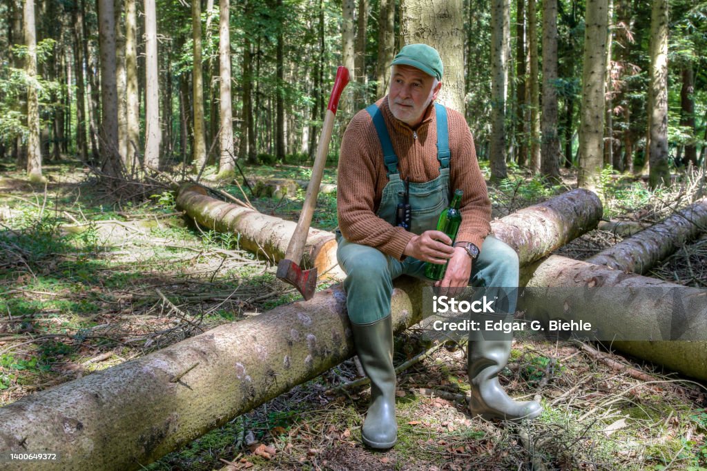 Work break in the forest. A lumberjack sits contentedly on a log in the forest next to his ax and takes a break from work.He enjoys the silence and tranquility in the forest. Lumberjack Stock Photo