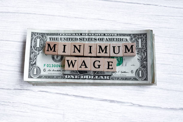 parola sul salario minimo scritta su blocco di legno con banconote da un dollaro americano. direttamente sopra. - minimum wage foto e immagini stock