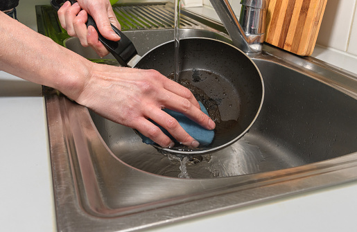 A woman tries to clean a burnt pan with her hands and a dishwashing sponge