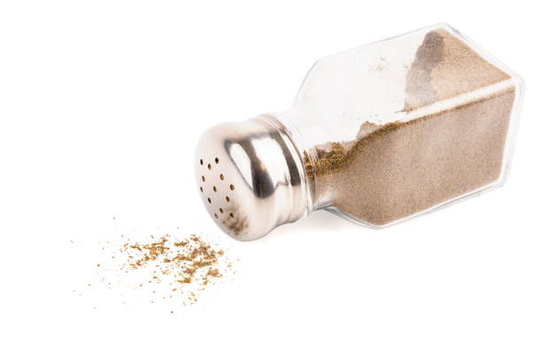 glass pepper pot with powdered black pepper inside dropped on its side isolated on white background, some pepper spilled