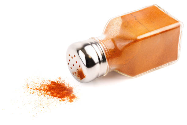 glass pepper pot with powdered red pepper inside dropped on its side isolated on white background, some pepper spilled