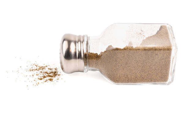 glass pepper pot with powdered black pepper inside dropped on its side isolated on white background, some pepper spilled