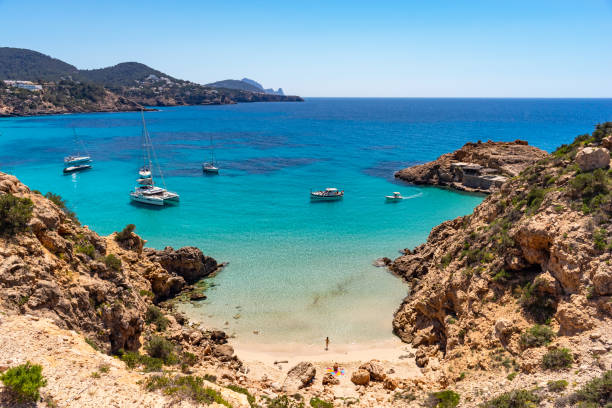 Cala Tarida, Platja des Pujolets, Beach, Cove, Ibiza, Spain Wide-angle view of the cove of Platja des Pujolets, near Cala Tarida, on the western coast of Ibiza, fishermen's huts, warm light, a few boats rocking on transparent waters, the gentle splashing of the waves on the shore. Developed from RAW. ibiza island stock pictures, royalty-free photos & images