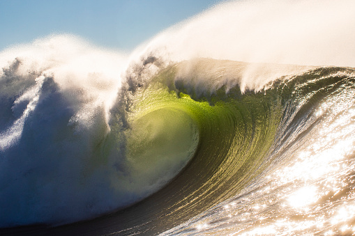 Powerful open ocean wave generated by storm swell barrelling on a shallow reef in bright morning sun light