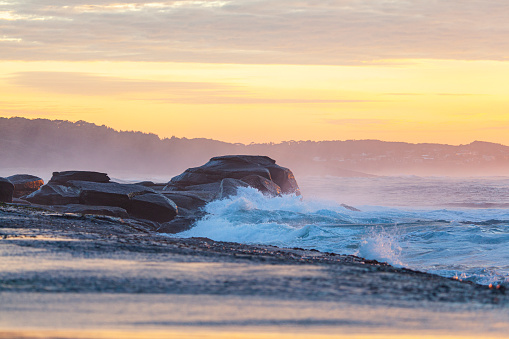 Coastal seascape scene of rocks and tidal waves surging with soft golden dramatic sky at sunrise