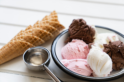 Summer ice cream buffet with a variety of ice cream flavors and sweet toppings. Overhead view table scene on a rustic white wood background.