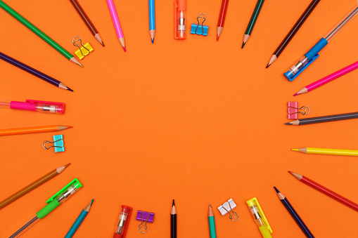 multi-colored pencils and pens forming a colored circle, isolated on an orange background