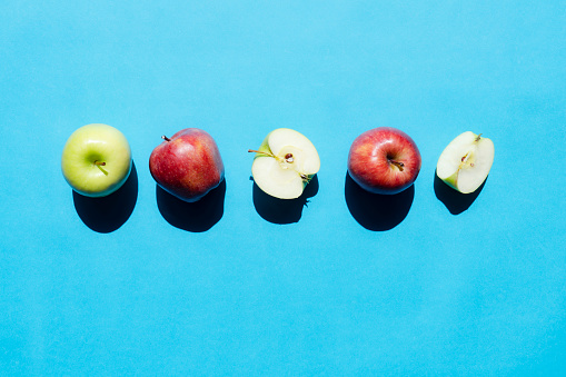 Green and Red Apples in a Row on Blue Background