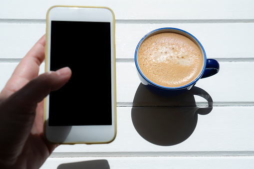 woman's hands holding smart phone and cup of coffee