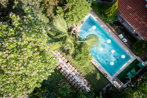 Aerial view of wedding reception and large dining table in garden of modern house with poolside lounge