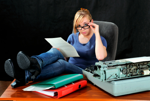 Businesswoman in eyeglasses with old typewriter. On dark background.