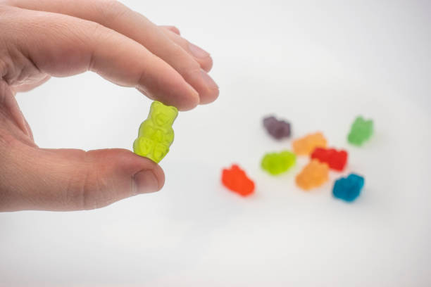 vista de uma mão masculina segurando uma goma de doce medicinal infundida cbd colorida usada para a cura - gummy - fotografias e filmes do acervo