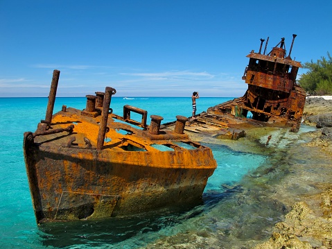 The wreck of an old abandoned ship lies by the shore of Grand Turk in Turks and Caicos on a bright sunny day.