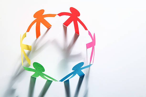 Paper cutouts of colorful people holding hands in a circle stock photo