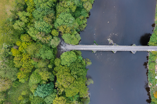 Aerial view from a drone of an old narrow stone bridge crossing a river in rural Scotland