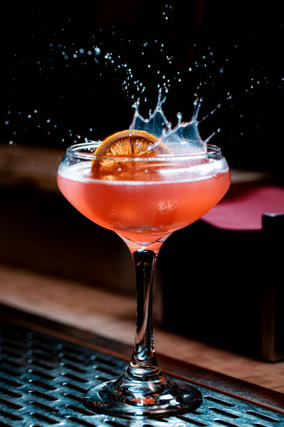 lemon garnish splashing in pink craft cocktail coupe glass - action alcohol alcoholism bar imagens e fotografias de stock