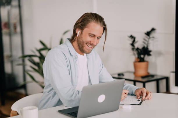 istock Distant studying by video conference. Focused young man student getting remote education. Male trainee sitting in headphones by laptop listening taking notes of real time class online 1400682562